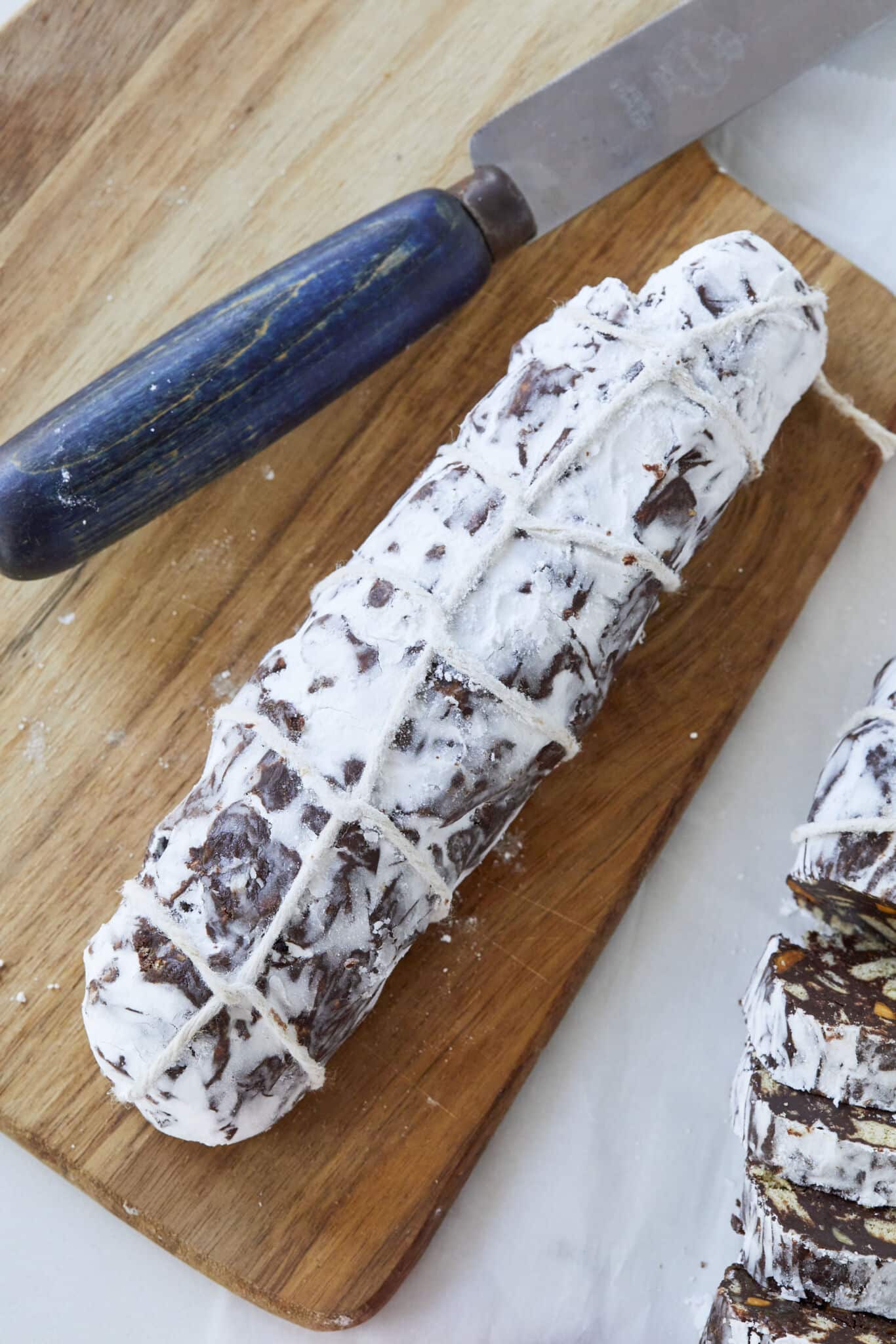 Italian Chocolate Biscuit Cake , also known as chocolate salami, is shaped into a log, resembling a salami, and is rolled in powdered sugar or cocoa powder to simulate the look of cured meat wrapped with twine around. 