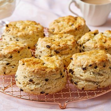 Golden, thick traditional Irish scones on a wire rack, served with jam, butter, and tea on the side.