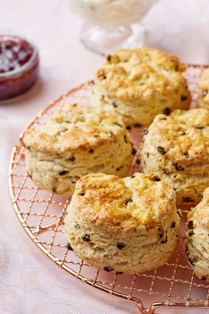 A close-up shot at thick golden brown scones on the wire rack, with jam in the back.