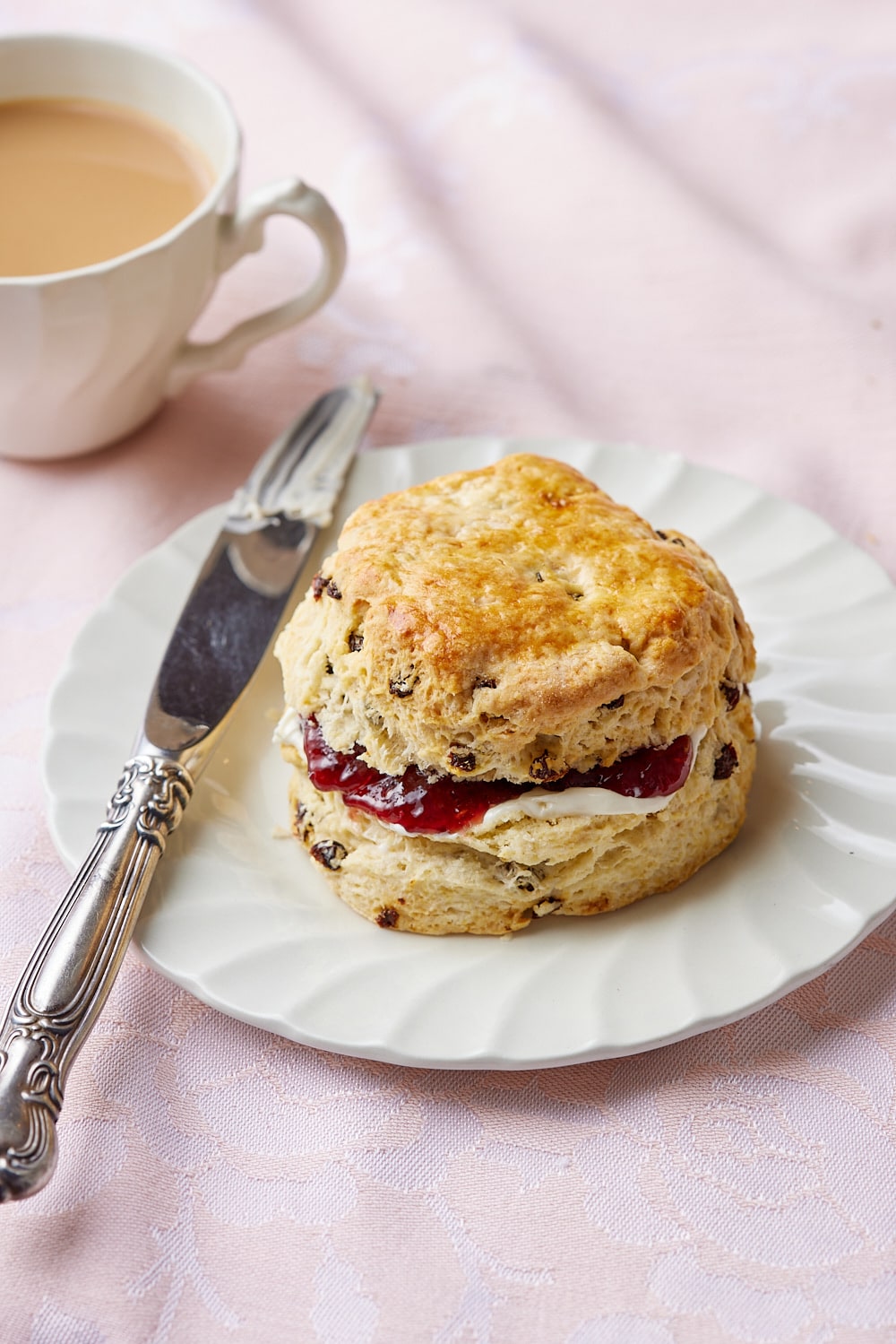 A traditional Irish scone stuffed with jam and butter on the plate, served with a cup of tea. 