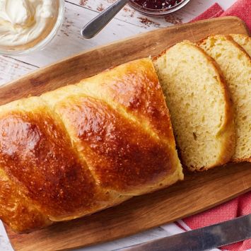A loaf of golden Brioche Bread with three slices cut off on a wooden board.