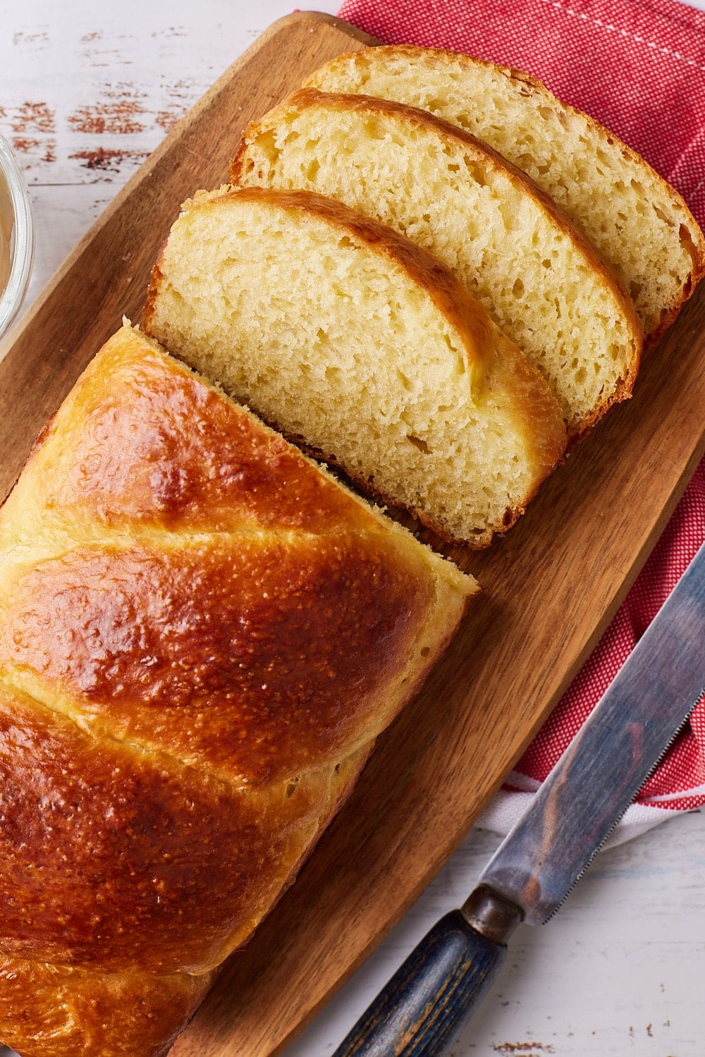 A loaf of golden brioche bread with three slices on a wooden board.