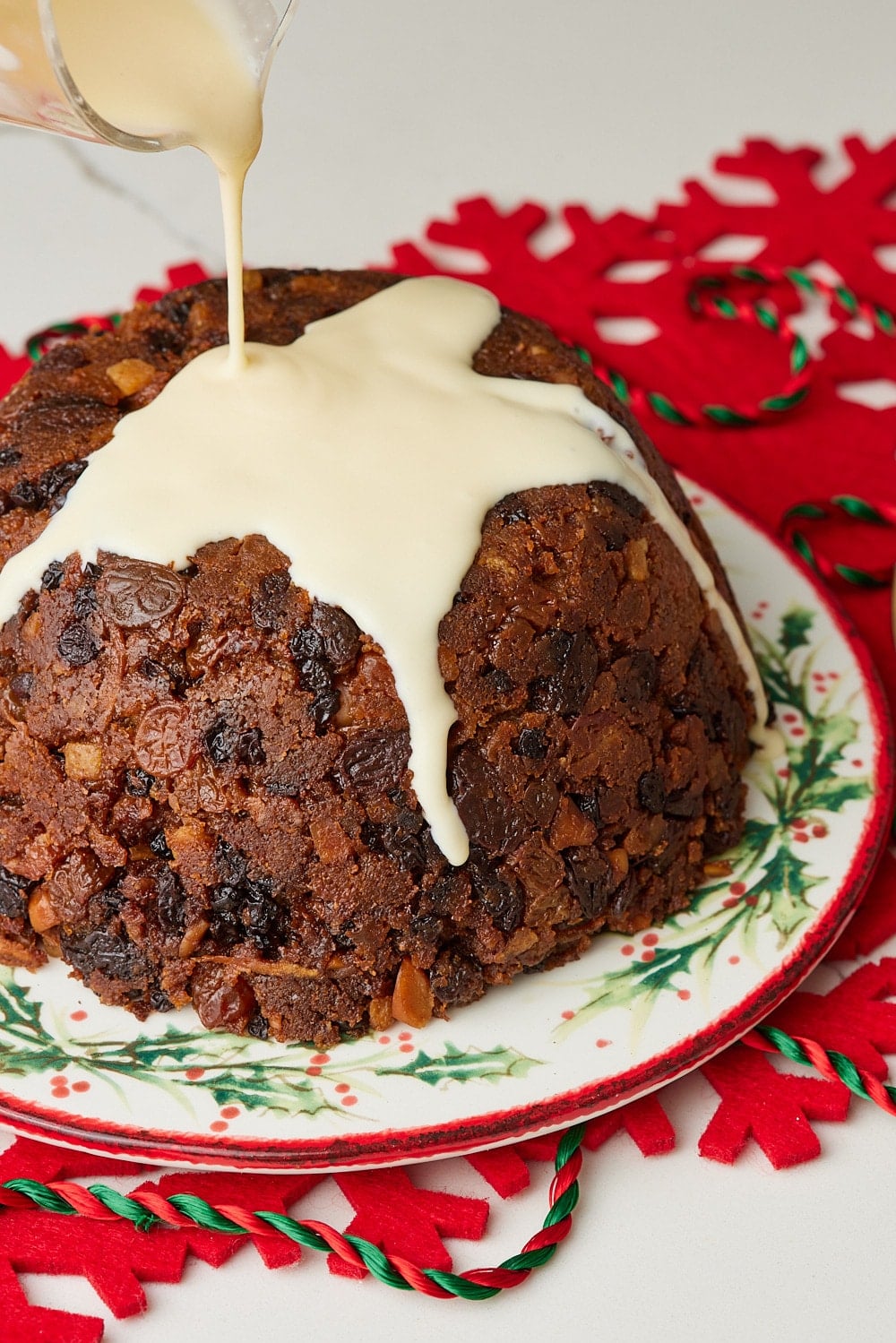 Christmas Pudding11 Christmas pudding topped with creamy custard sauce being poured over the rich, fruit-filled pudding.