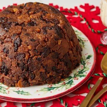 Traditional Christmas pudding packed with dried fruit and candied peel, served on a festive Christmas plate with custard and gold spoons.