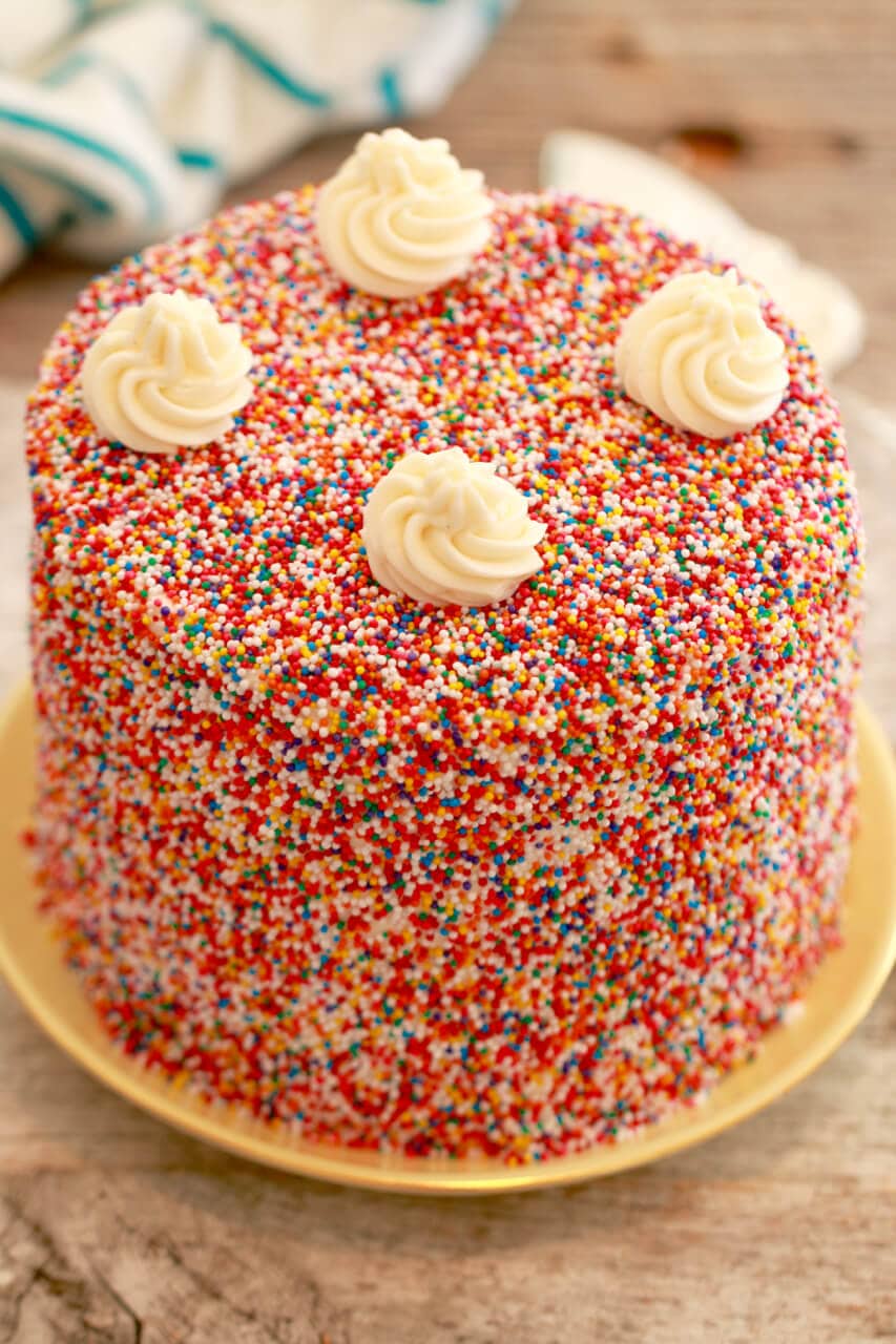My Vanilla Birthday Cake Recipe with Buttercream Frosting covered in sprinkles.