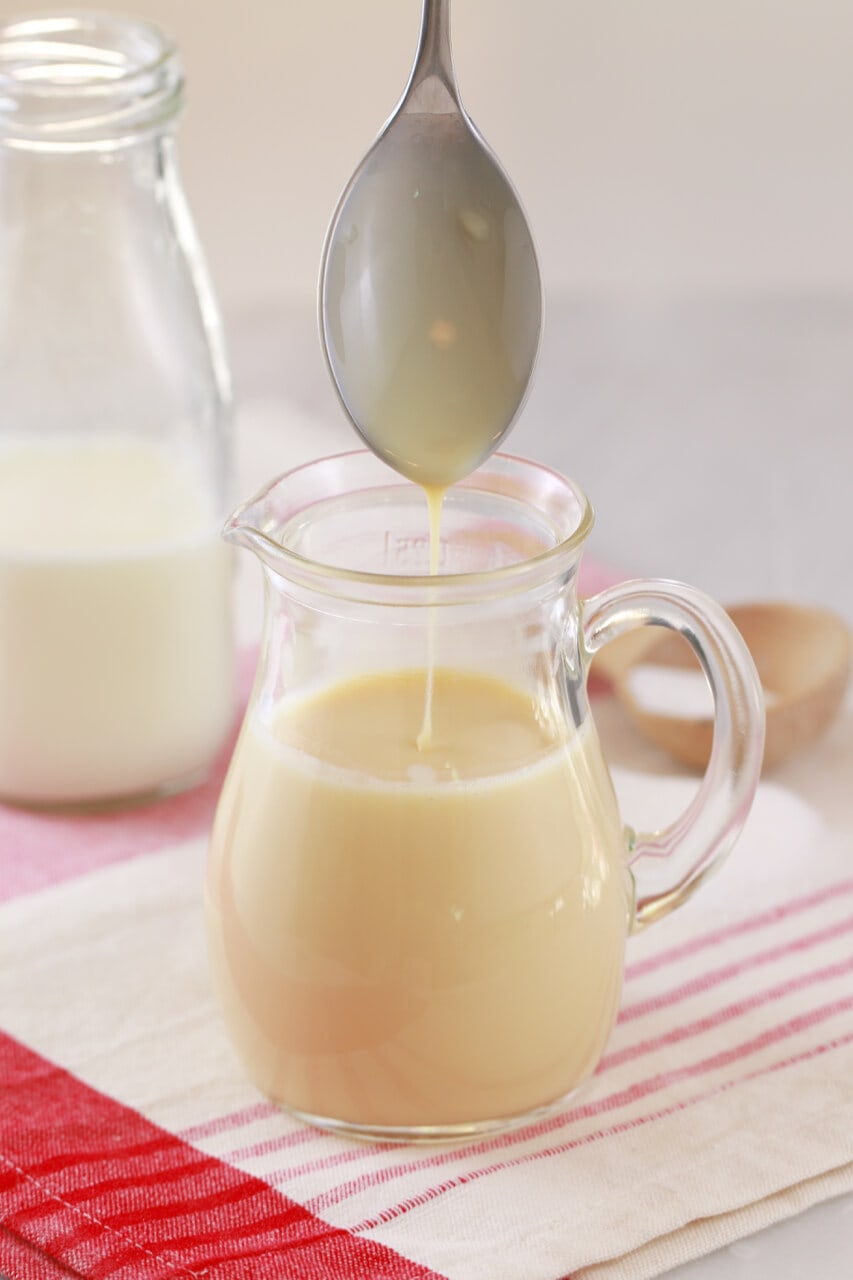 Sweetened Condensed Milk from the easiest Homemade Ice Cream Recipe is in a glass jar with a condensed milk coated spoon hovering over.