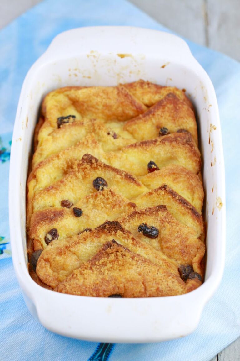 Homemade Irish Bread and Butter Pudding with raisins is presented in a white baking dish. 