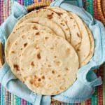 Top down view od cooked homemade flour tortilla placed in a basket lined with a clean tea towel.
