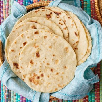 Top down view od cooked homemade flour tortilla placed in a basket lined with a clean tea towel.
