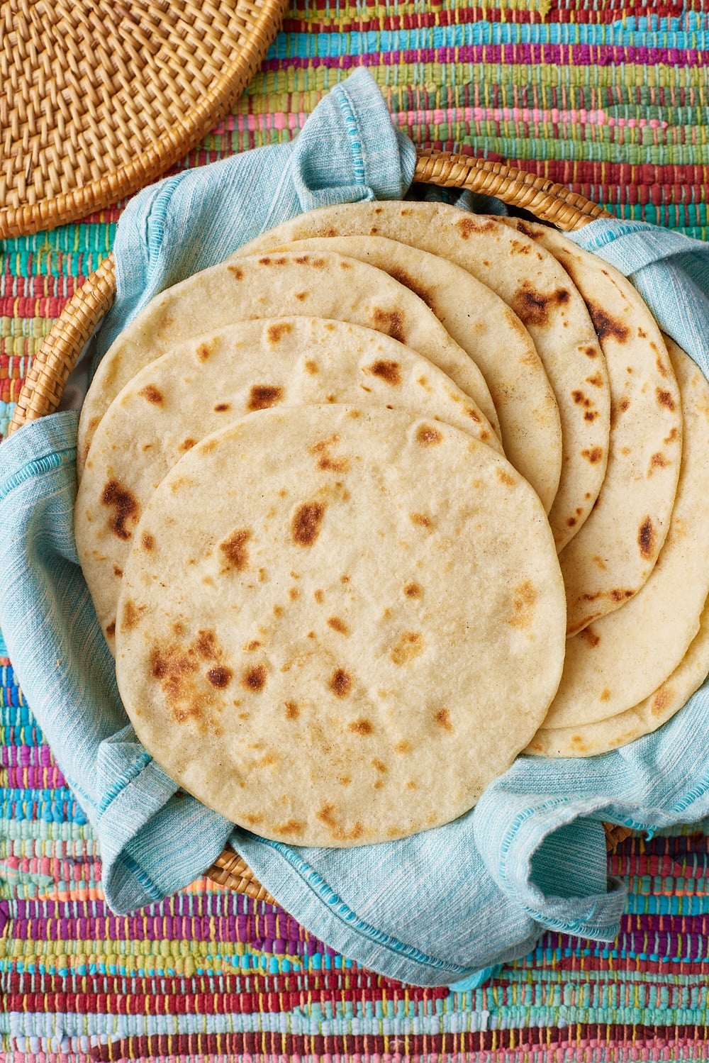 Cooked homemade flour tortilla placed in a basket lined with a clean tea towel. 