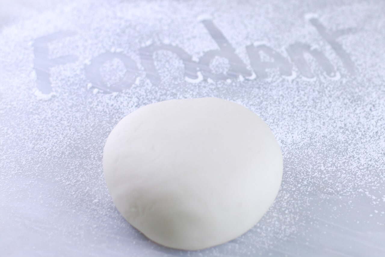 A ball of rolled fondant with the word "fondant" written above it in flour.