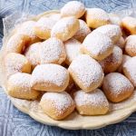 A heaping plate of lightly golden, fluffy Beignets dusted with powdered sugar.