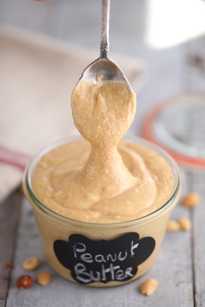 A spoon dripping homemade peanut butter.