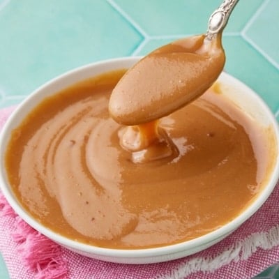 A bowl of glossy, homemade dulce de leche with a spoonful drizzling over the rich caramel sauce.