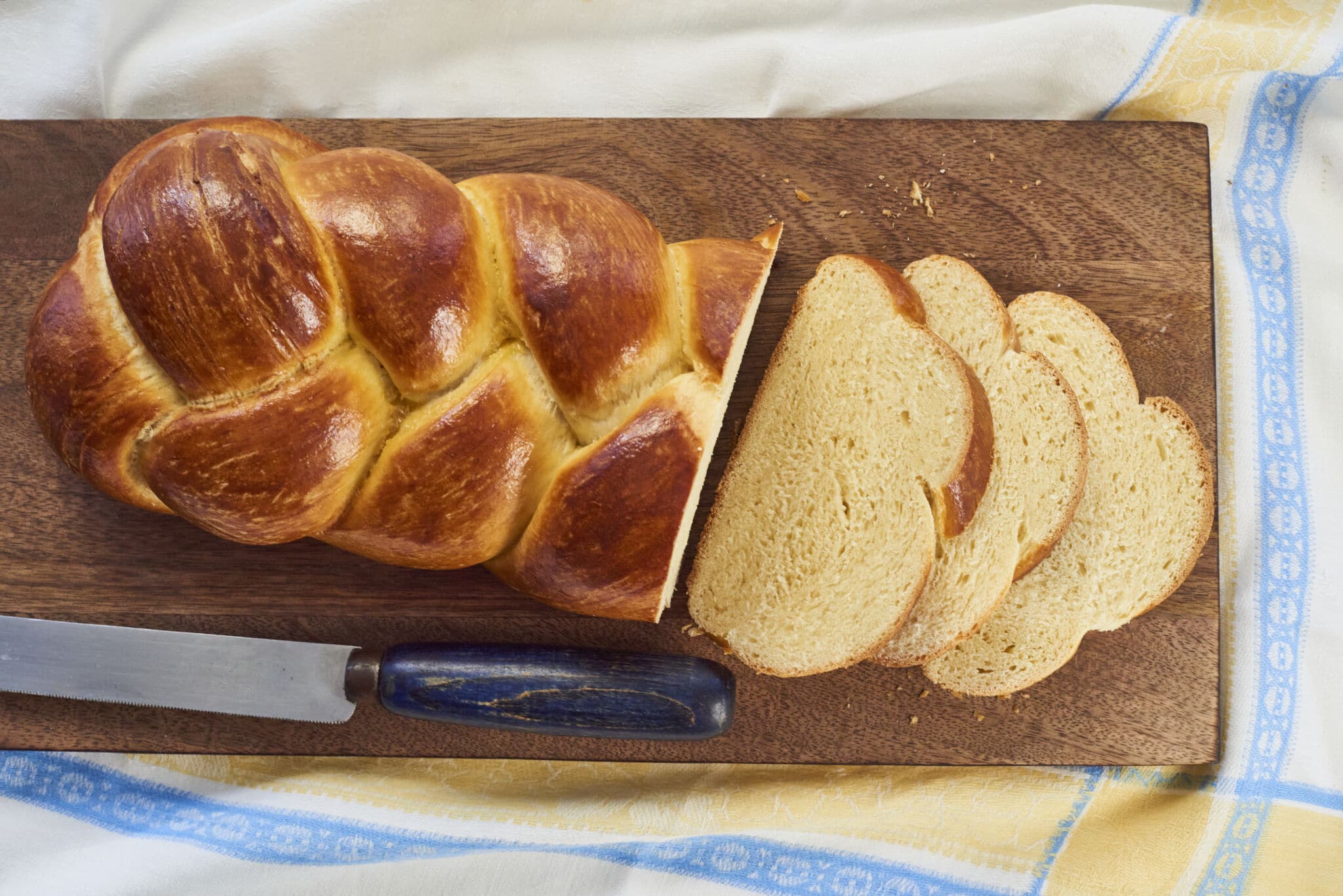 A loaf of homemade Challah bread is served on a cutting board. Three slices have been made in the loaf.