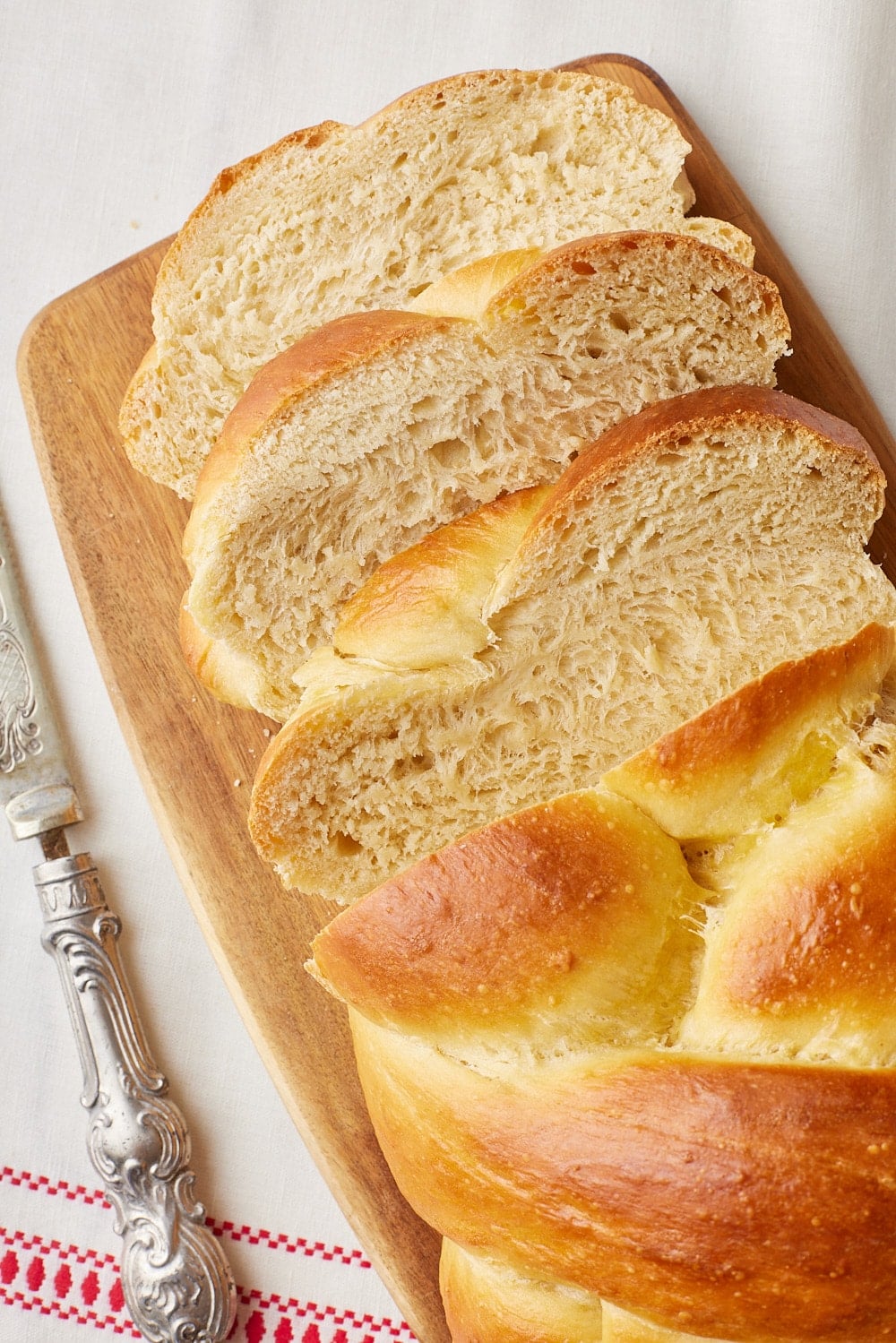 No-knead Challah11 Golden braided challah bread sliced on a wooden board, showing its soft, fluffy interior and golden crust.