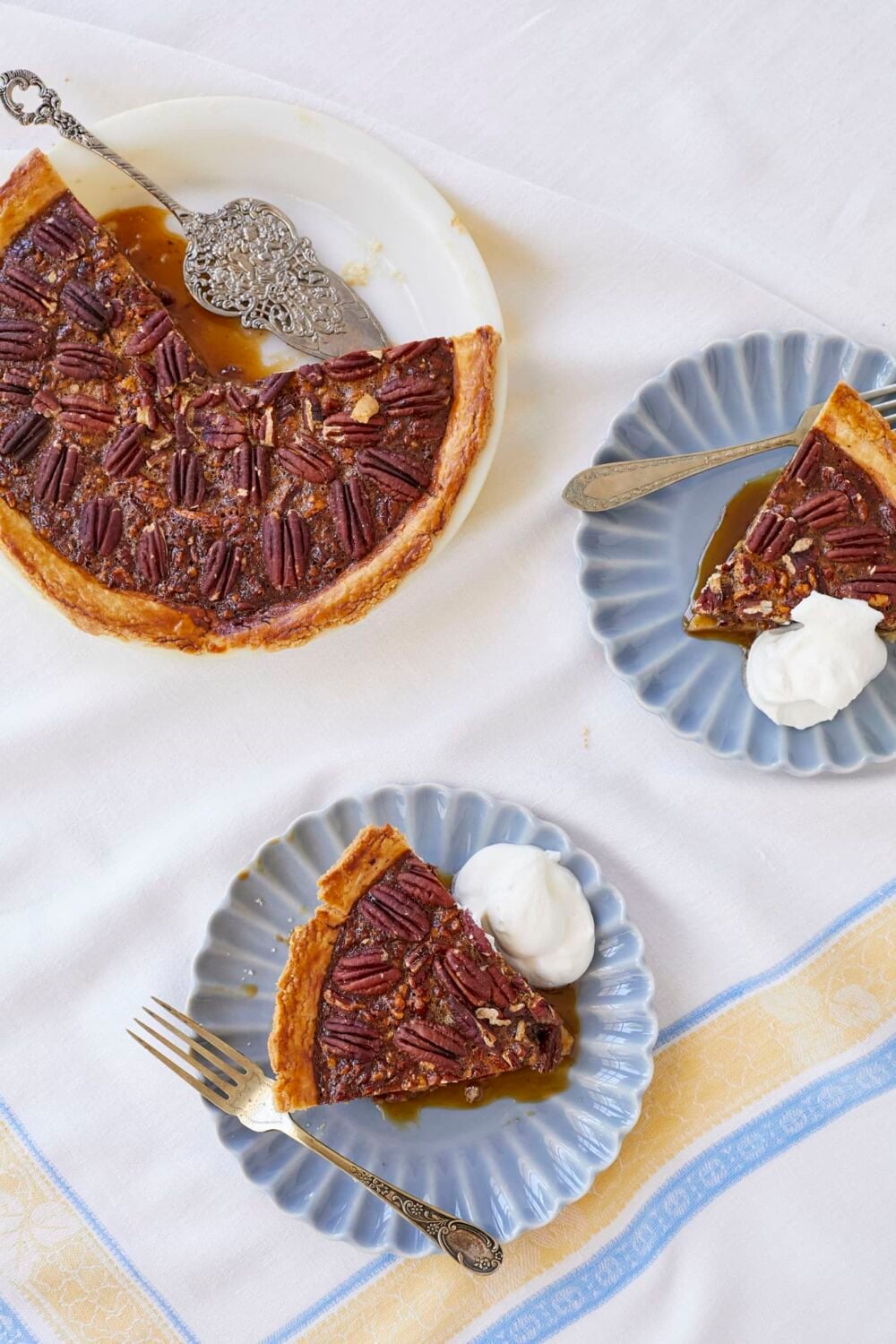 Best Ever Pecan Pie2 Top down view of two slices and the rest of the pecan pie, served with softly whipped cream on top.
