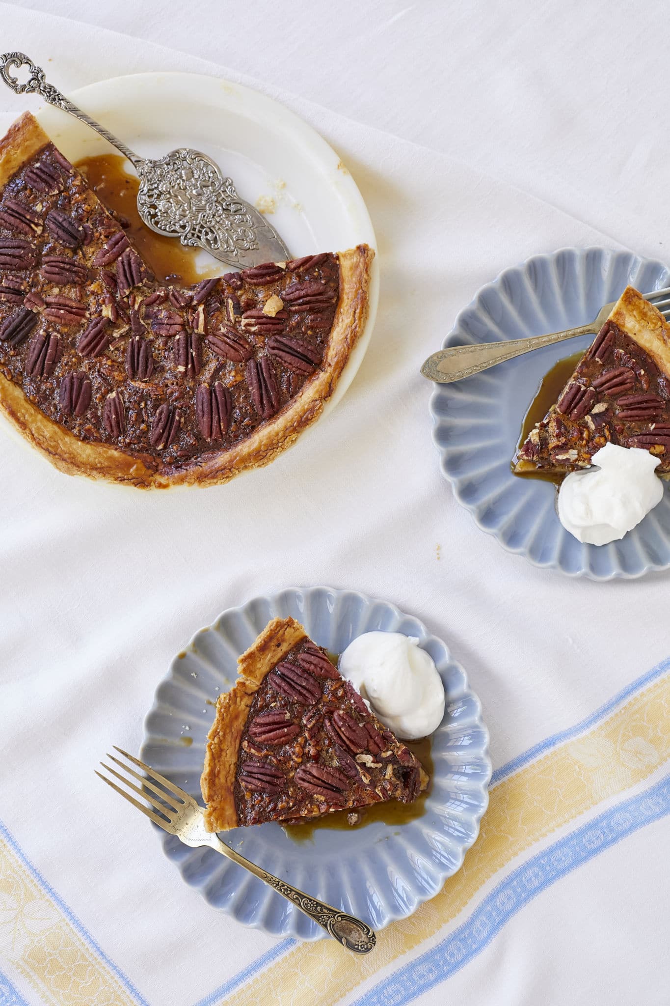 An overhead shot of pecan pie in the baking tin with two slices served on blue plates with homemade whipped cream.