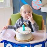 A baby with a smash cake and a candle that's the number one.