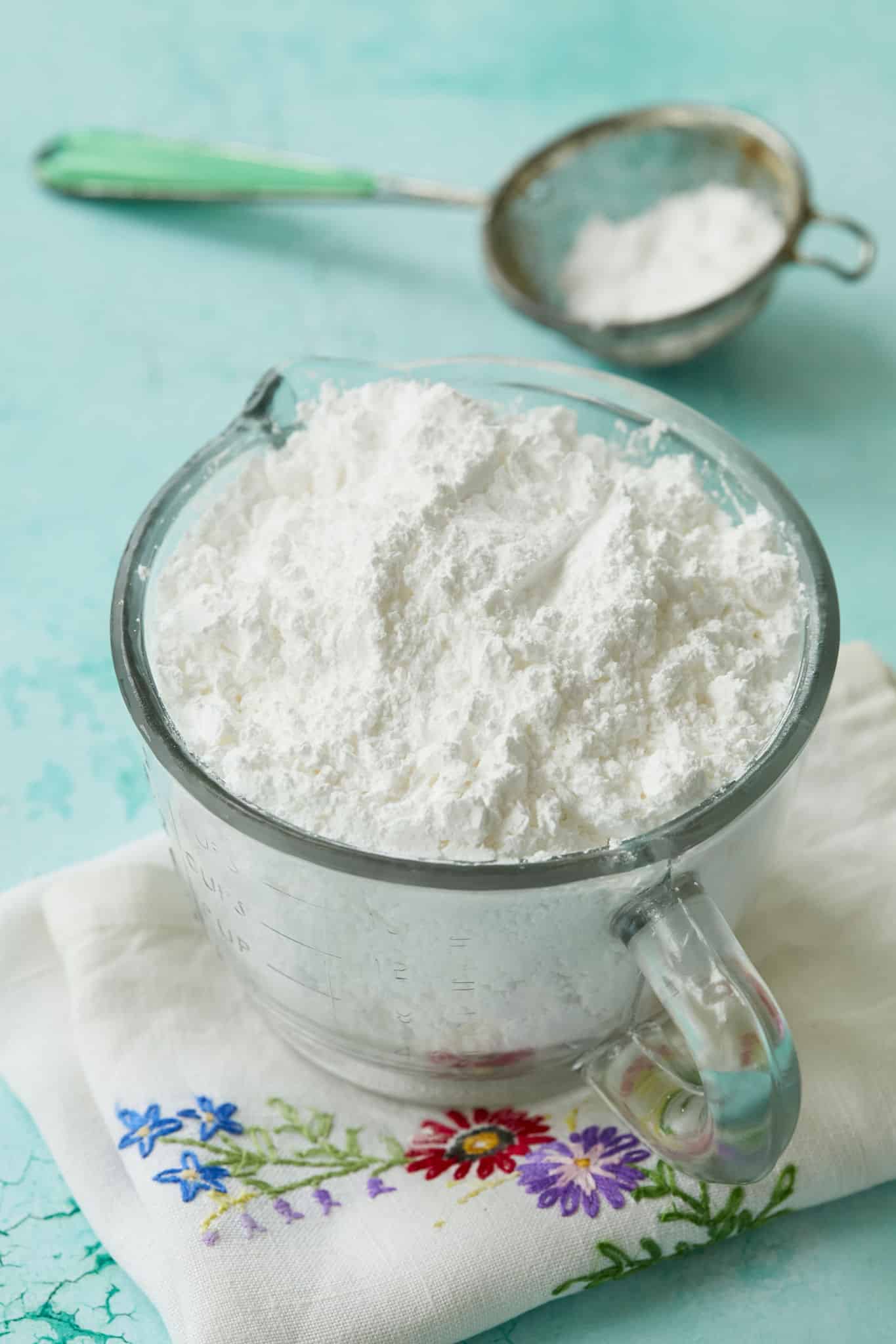 A measuring cup of homemade powdered sugar is displayed on a tea towel.