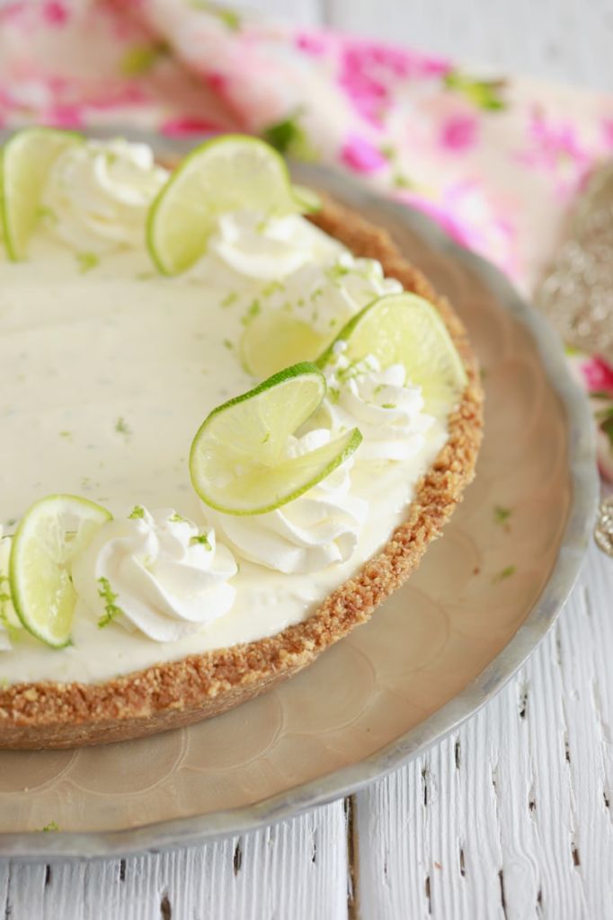 Key lime pie on a platter with whipped cream and lime slices.