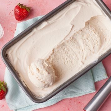 A tin of strawberry I ce cream with fresh strawberries on the side.