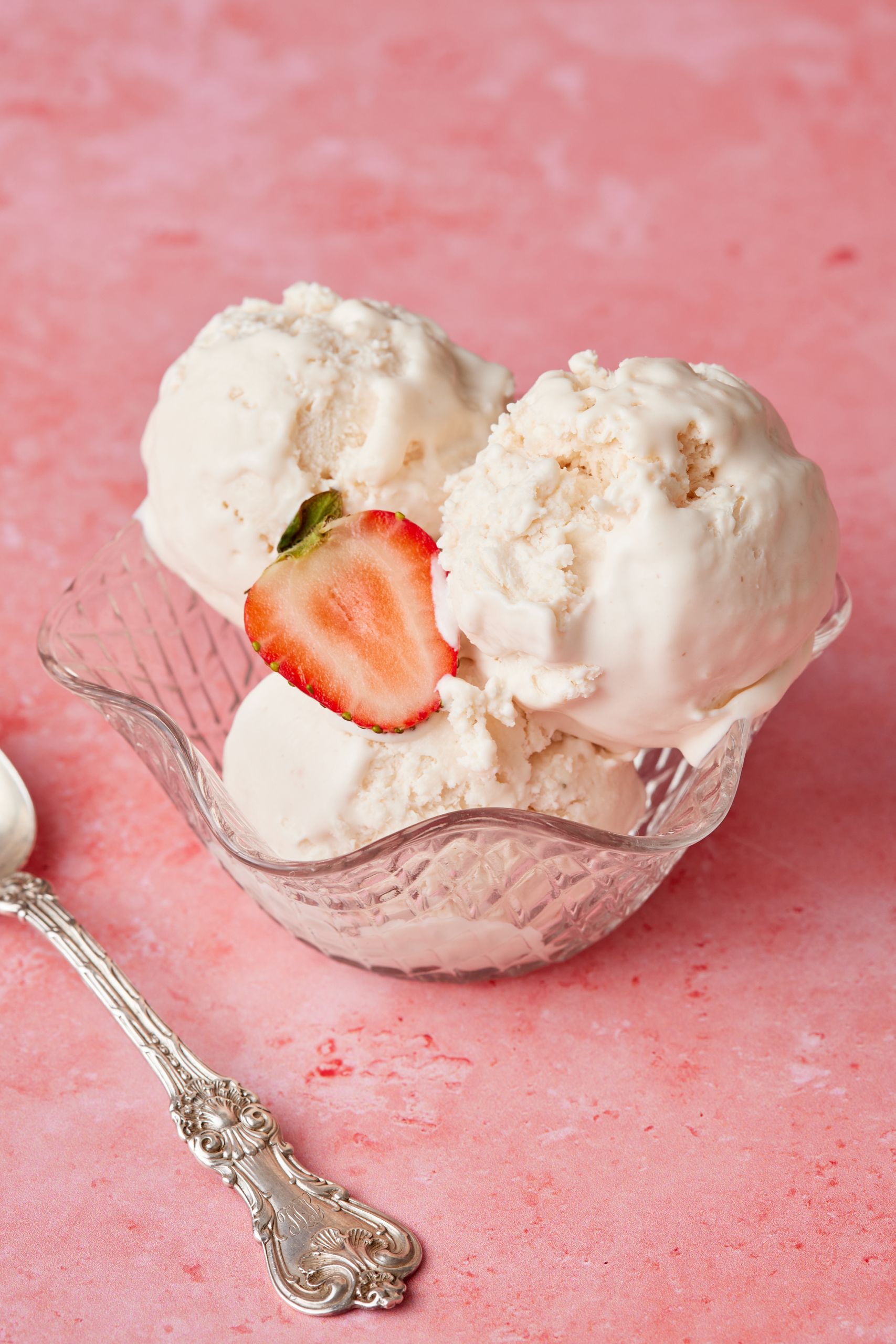 Three scoops os strawberry ice cream served in a glass bowl with fresh strawberry slice. 
