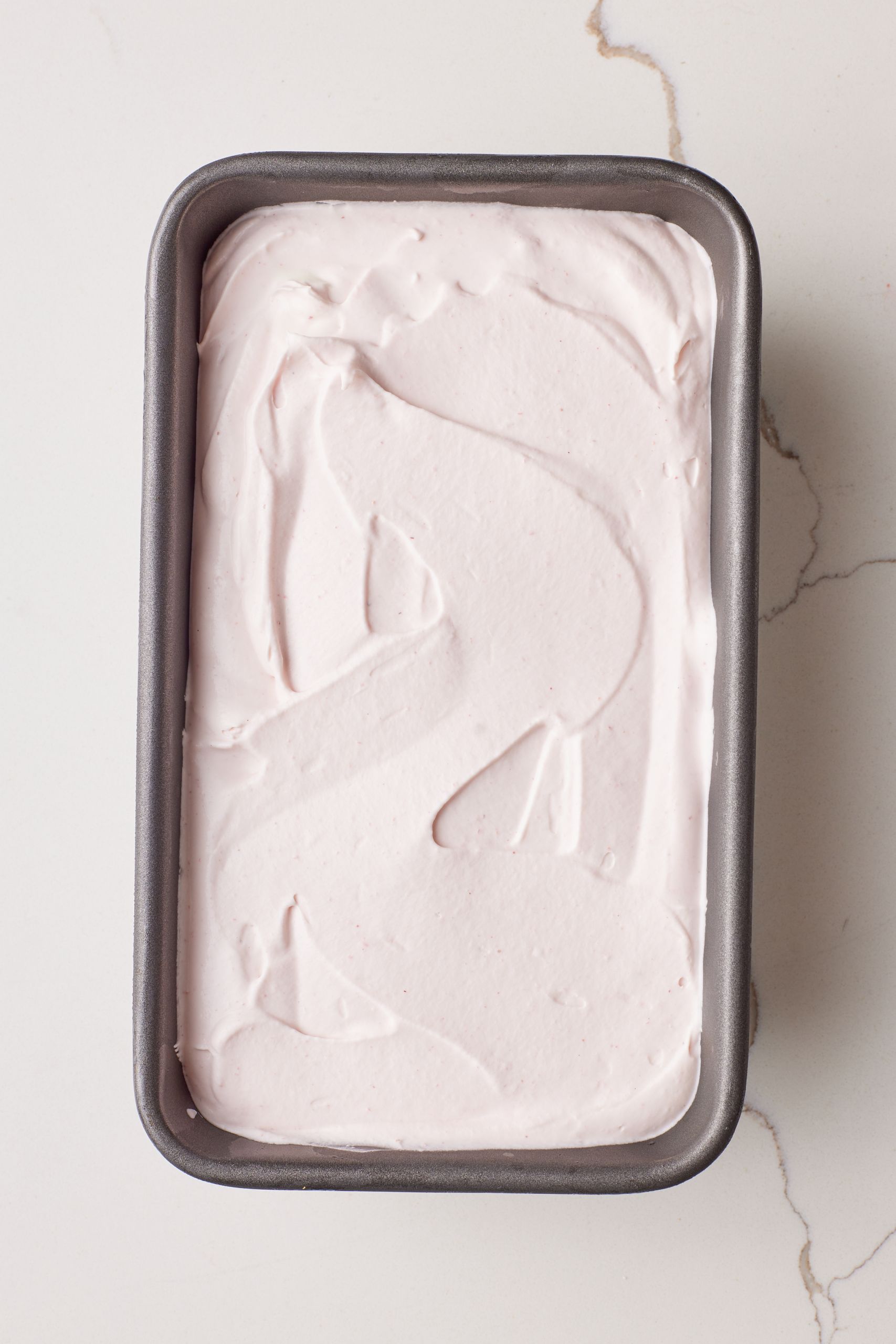 A top-down view of strawberry ice cream (no-churn) in a loaf tin. 