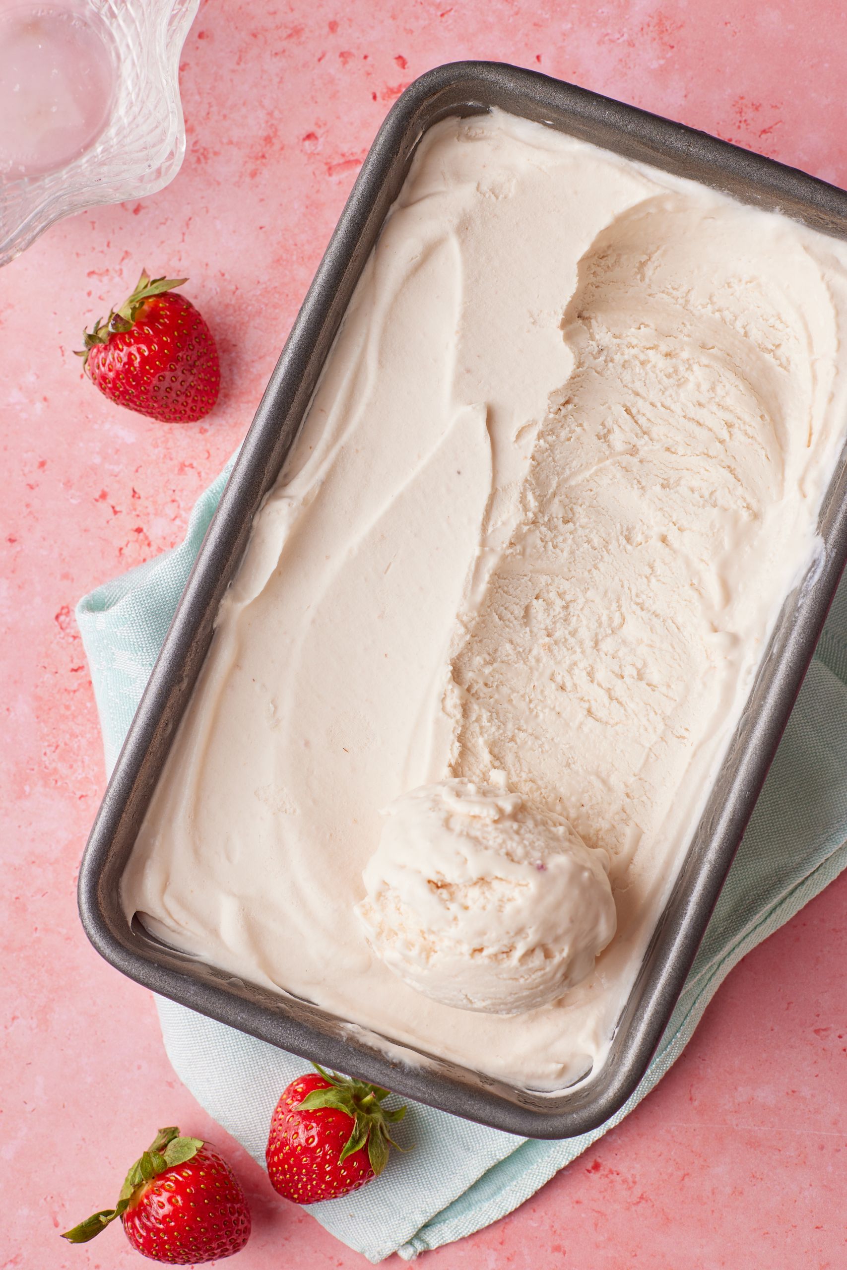 No-churn strawberry ice cream in a metal loaf tin with one scooped ice cream ball. Fresh strawberries are on the side. 