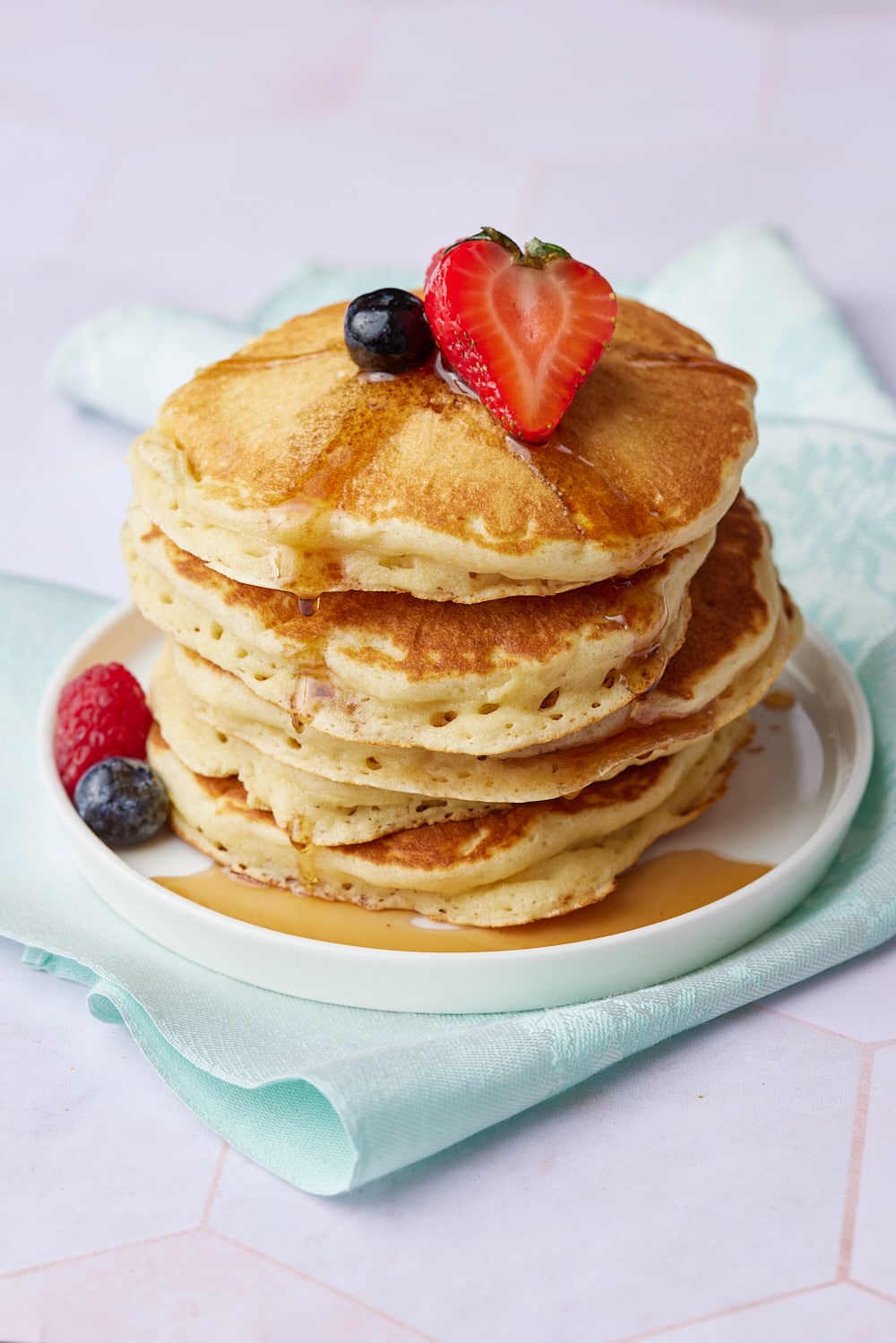 A stack of fluffy homemade pancakes topped with strawberries and blueberries. 