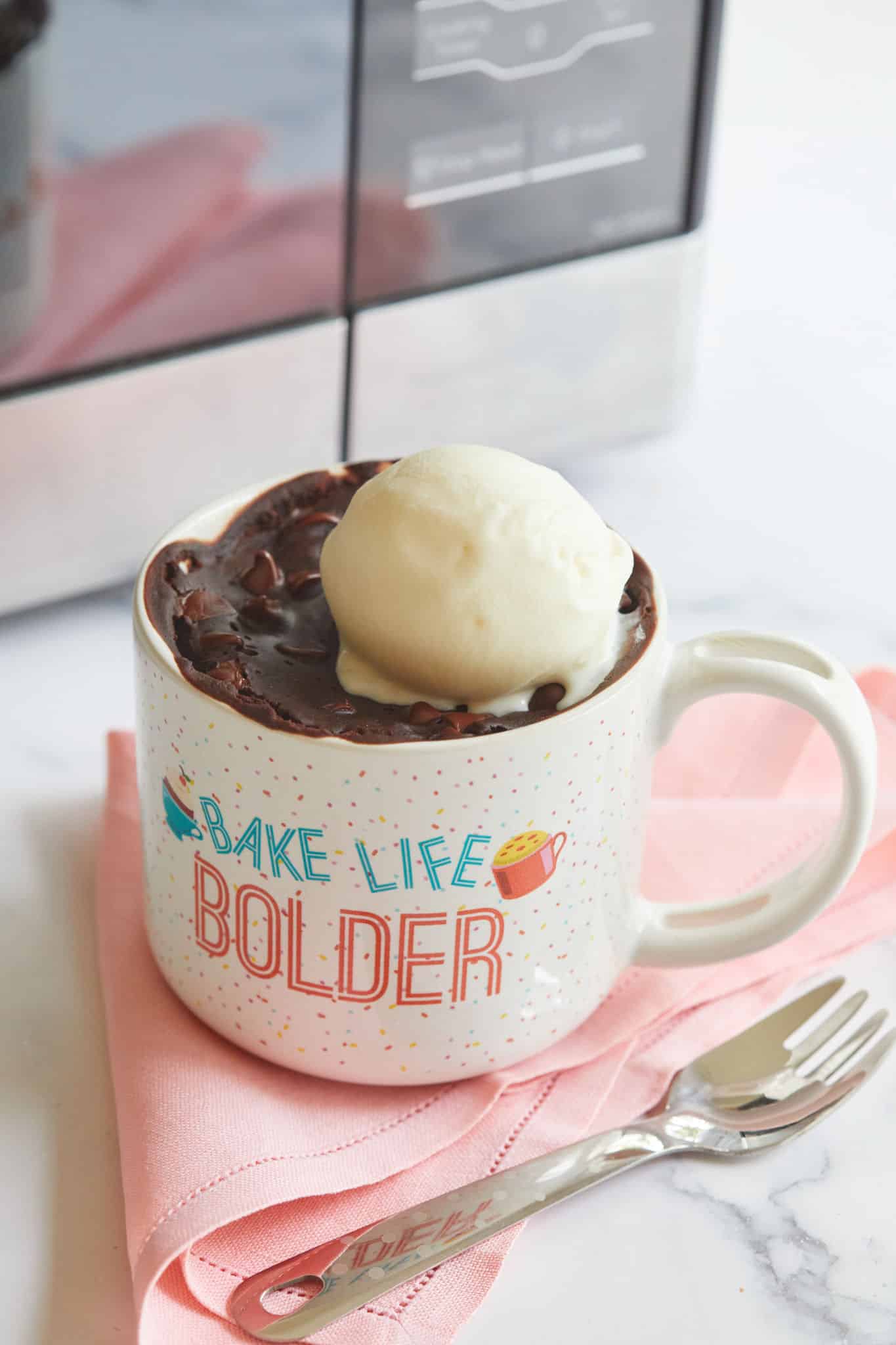 A brownie made in the microwave, sitting on a pink napkin and topped with ice cream.