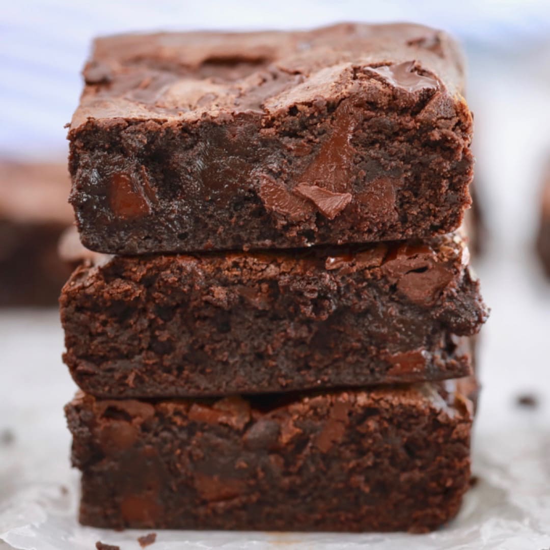 A close-up shot at a stack of Best-Ever Brownies shows the shinny crinkled top and the gooey center packed with melted chocolate. 