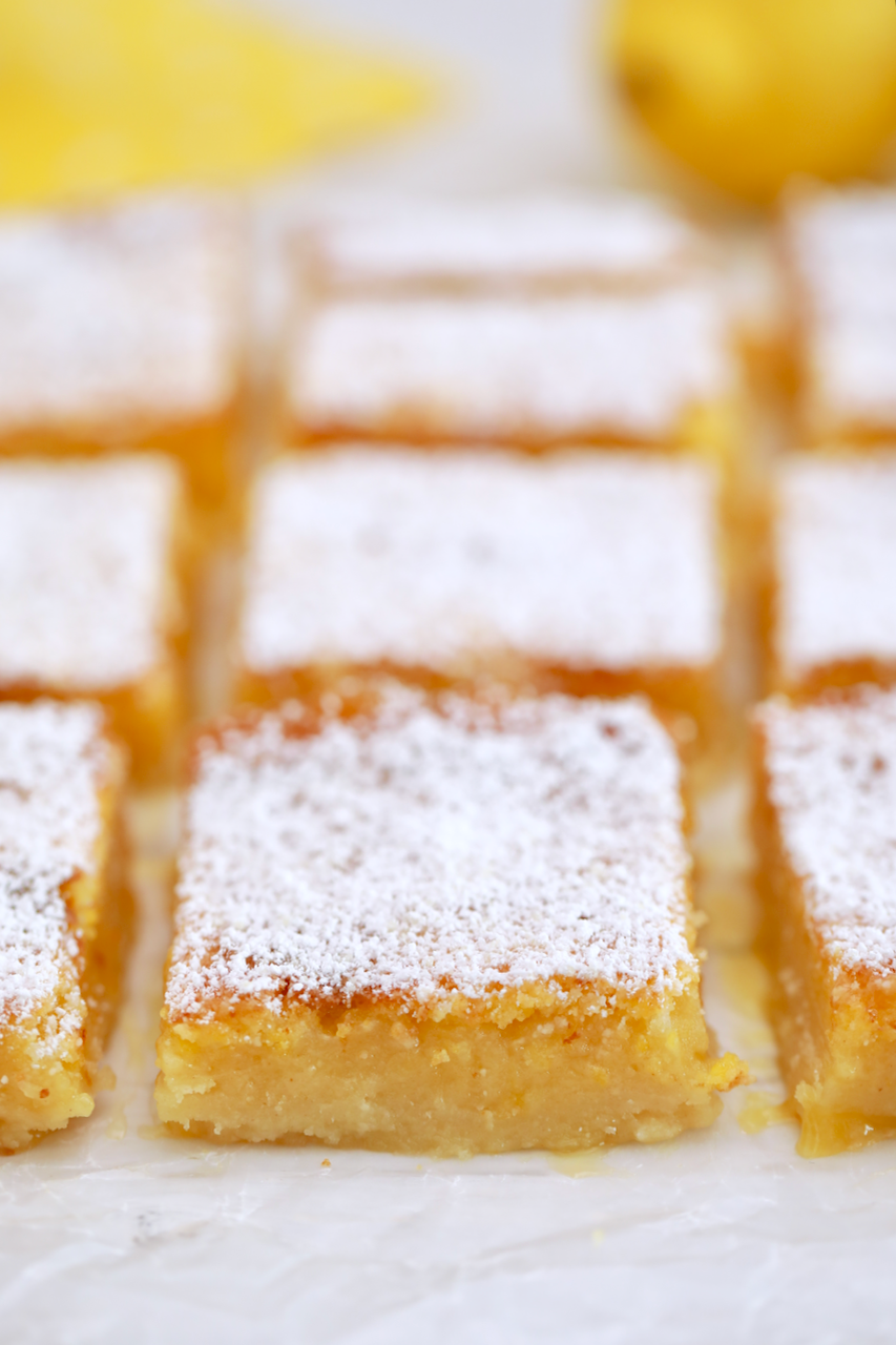 Rows of lemon bars dusted with powdered sugar on parchment paper.