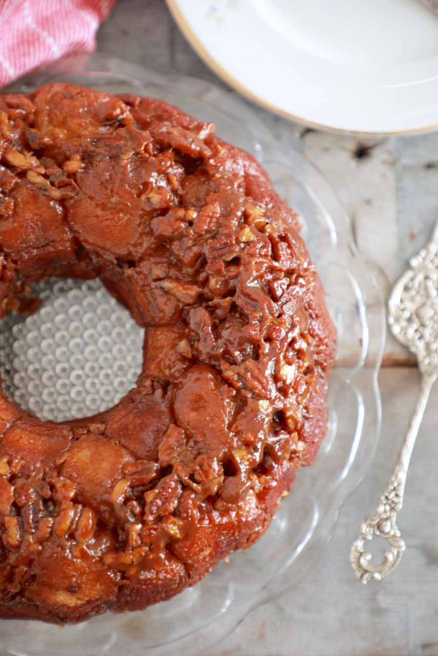 A bundt cake looking monkey bread is served on a table with pecans and caramel over the top.