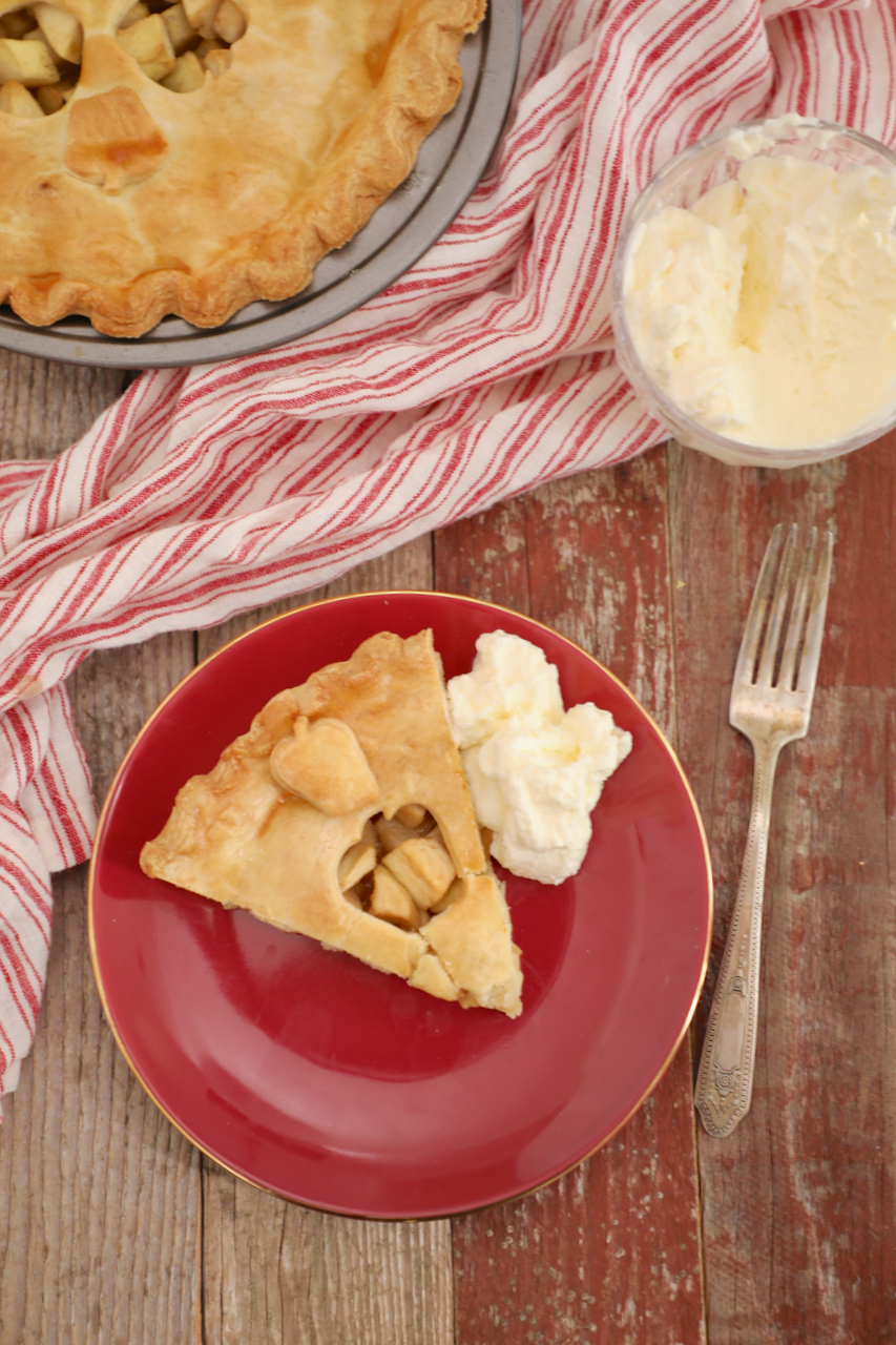 Homemade apple pie is served on a red dish with a side of whipped cream