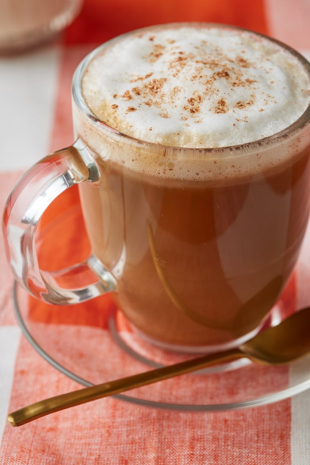 Pumpkin Spice Coffee Creamer6 Close-up of a pumpkin spice latte with frothy milk and cinnamon, served in a glass mug.