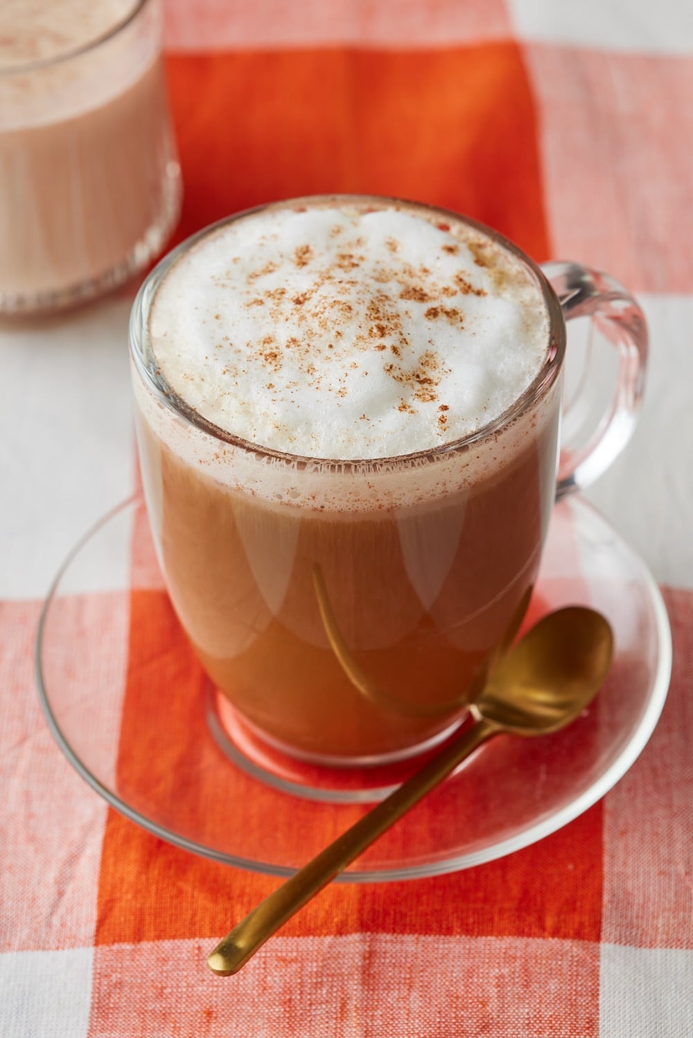 Pumpkin Spice Coffee Creamer7 Pumpkin spice latte topped with frothy milk and cinnamon, served in a glass mug with a spoon on a saucer.
