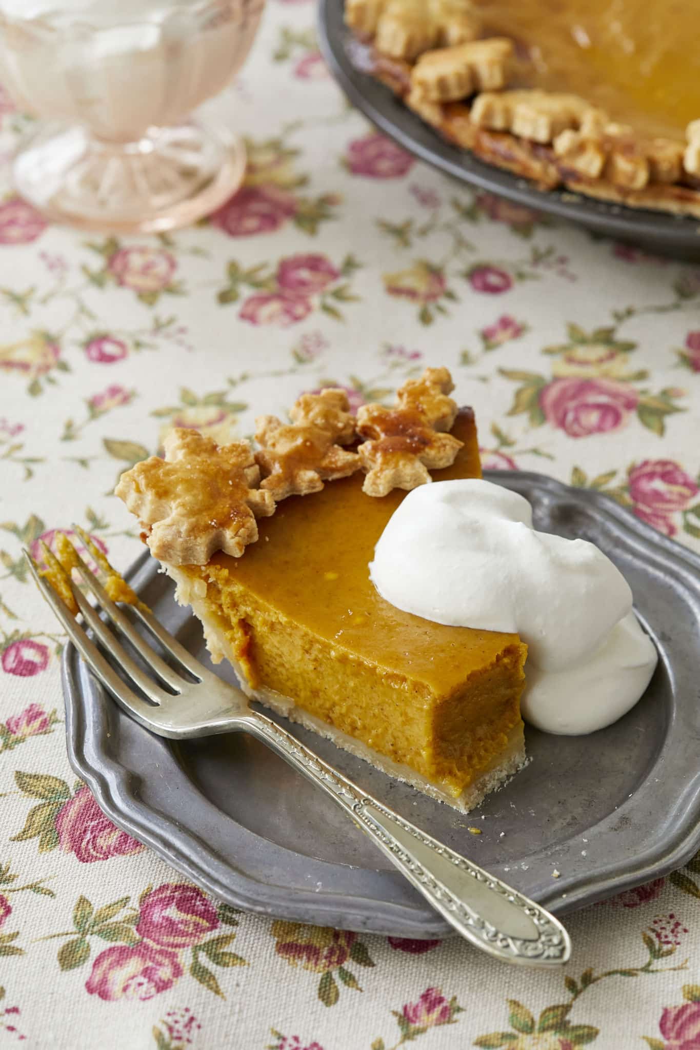 A picture of homemade pumpkin pie with homemade whipped cream is served on a silver dish; a bite has been taken from the tip of the pie.