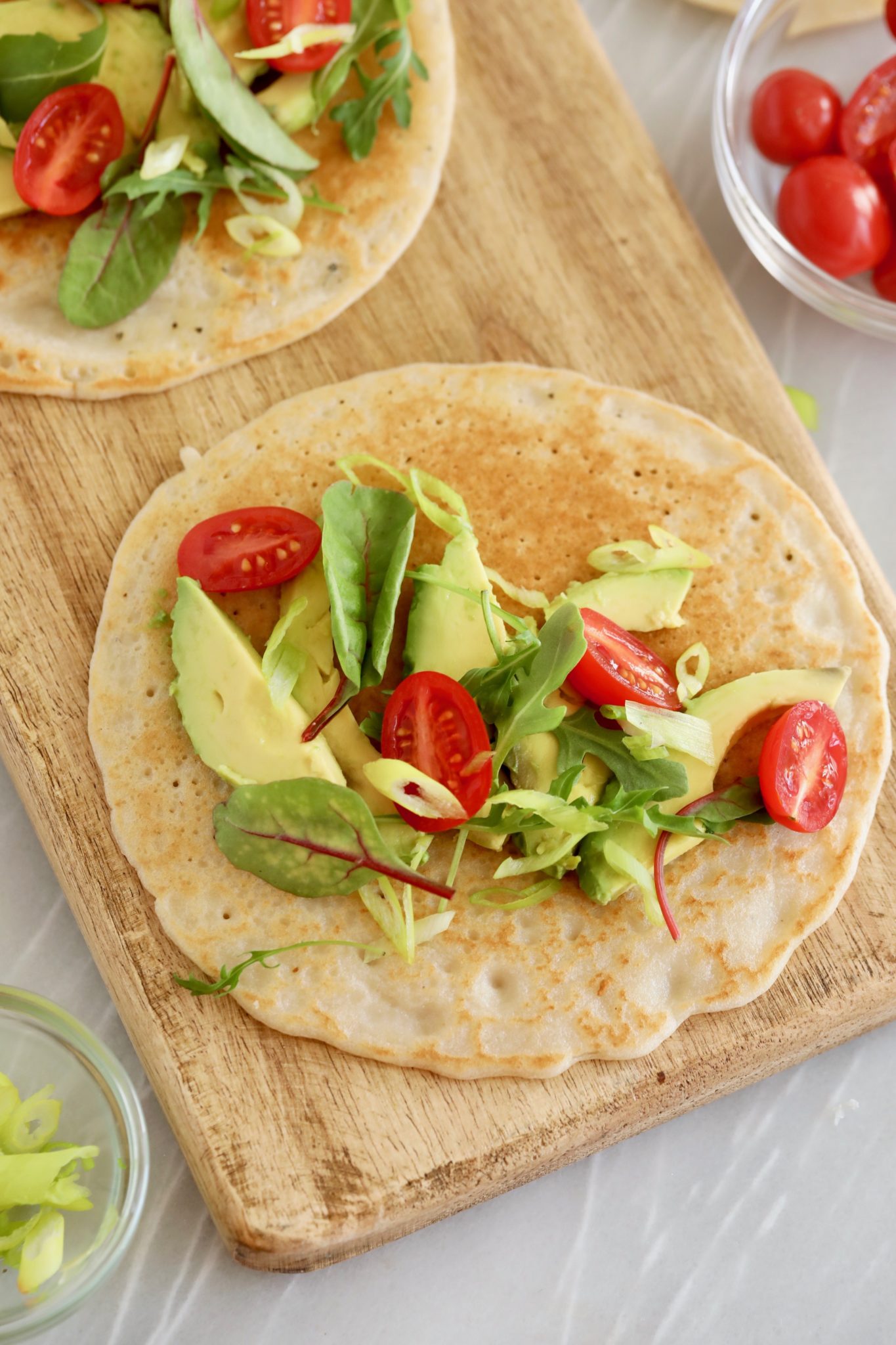 Two gluten-free flatbreads topped with veggies and avocado.