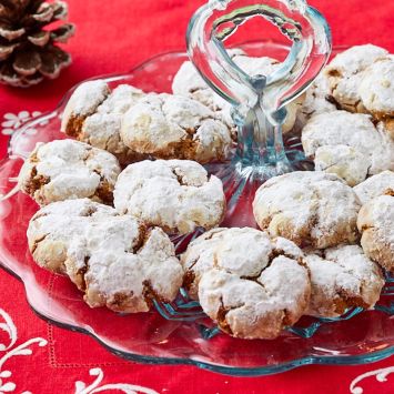 Ginger Crinkle Cookies are coated with powdered sugar and being displayed on a glass platter.