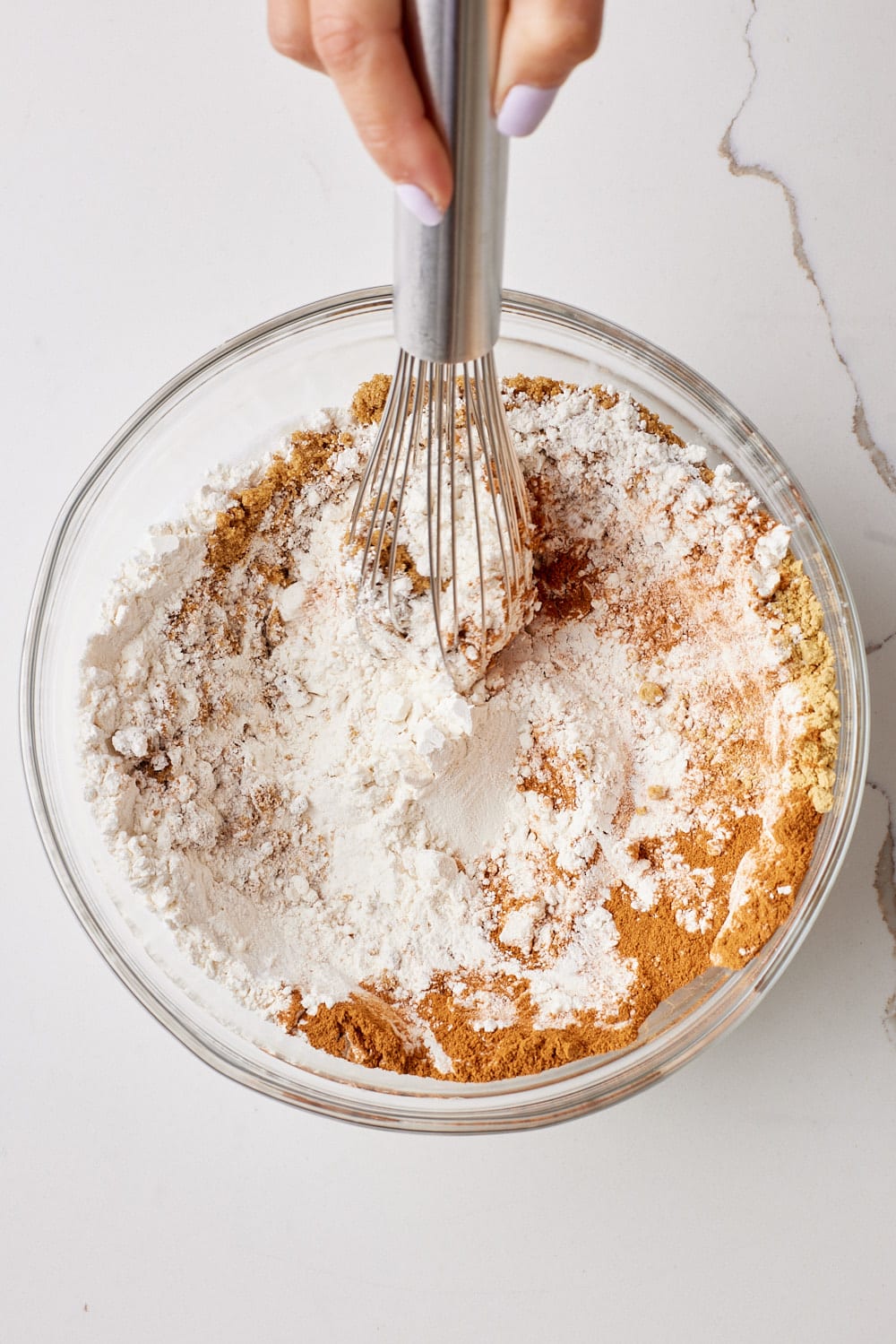 Dry ingredients of Ginger Crinkle Cookies mixed with a whisk in a glass bowl. 