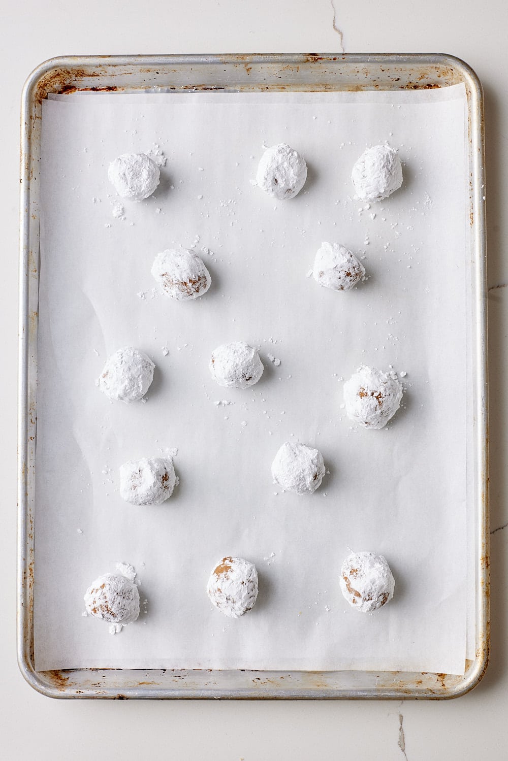 Arrange cookie dough balls coated with powdered sugar on the parchment-lined baking sheet. 