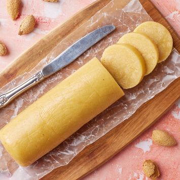 A log of Marzipan with three slices on a wooden chopping board.