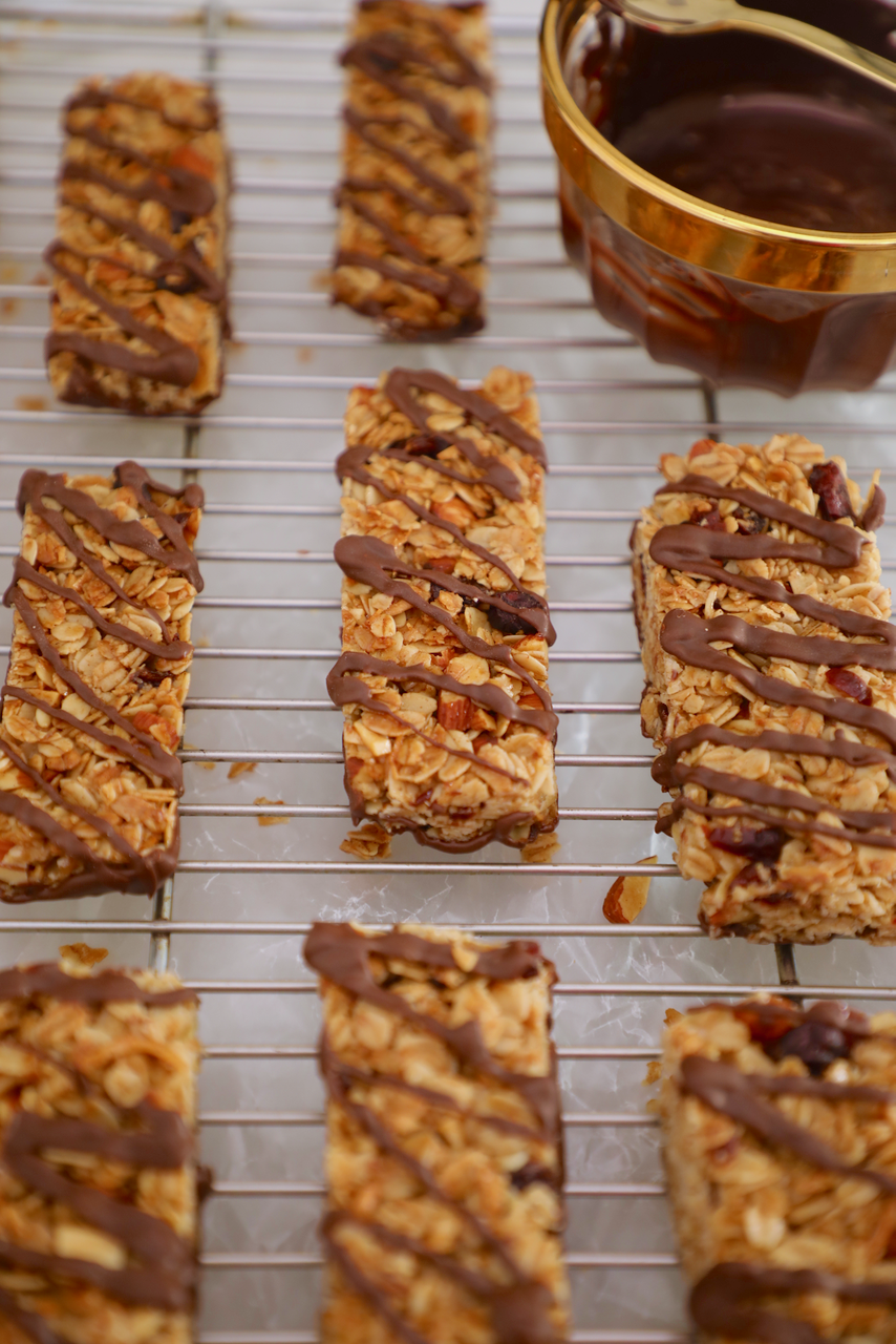 Homemade granola bars with chocolate sit on a cooling rack.