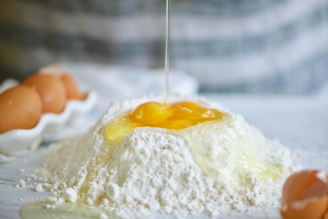 Fresh eggs being poured into a mound of flour.