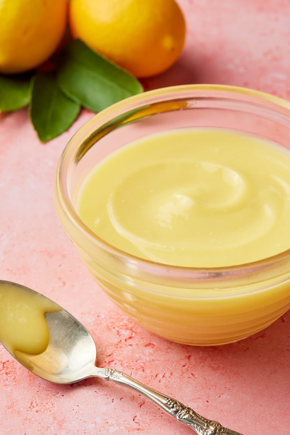 A bowl of silky smooth microwave lemon curd, with two fresh lemons in the bakground. 