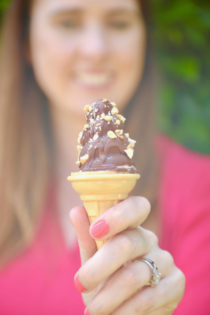 A drumstick ice cream cone being offered.