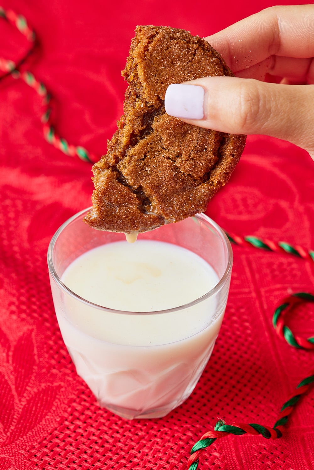 Half of a molasses cookie dipping into a glass of milk. 