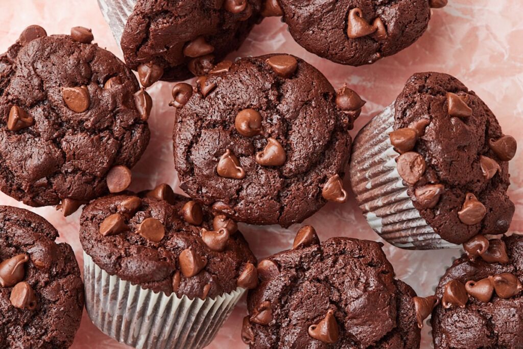 Top view of homemade bakery-style double chocolate chip muffins with domed tops and melty chocolate chips arranged on parchment paper.