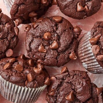 Top view of homemade bakery-style double chocolate chip muffins with domed tops and melty chocolate chips arranged on parchment paper.